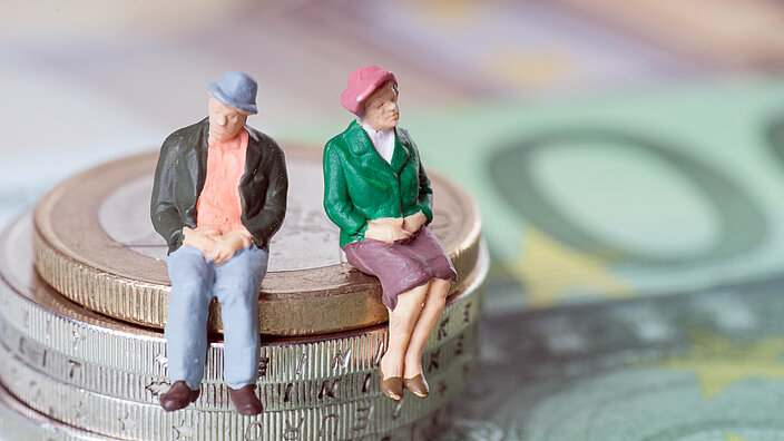 Spielfiguren von älteren Leuten sitzen auf Kleingeld