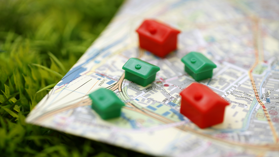 Nahaufnahme einer Stadtkarte mit Monopoly-Häuschen (Grün) und Hotels (Rot) drauf, welche auf einer Wiese liegt.