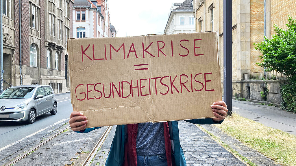 Ein Schild wird hochgehalten, Aufschrift: Klimakrise = Gesundheitskrise